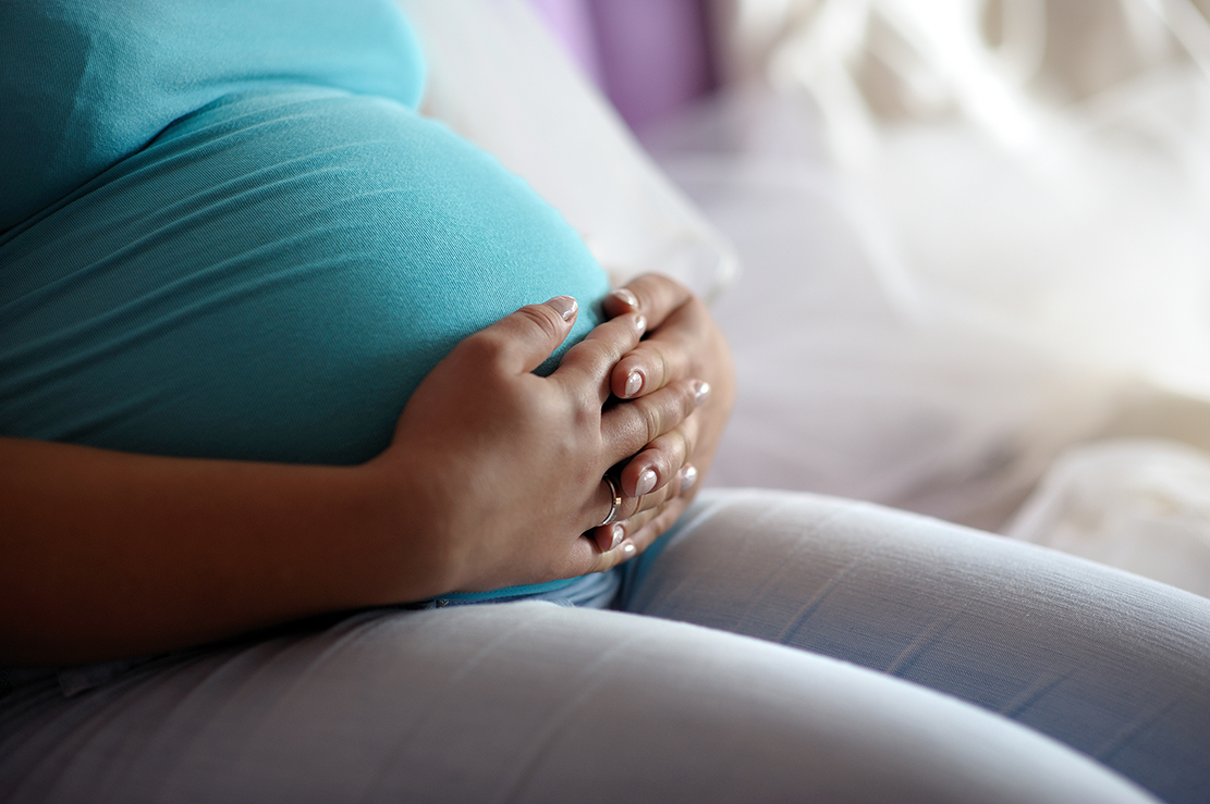 Pregnant person sits cradling their stomach. 